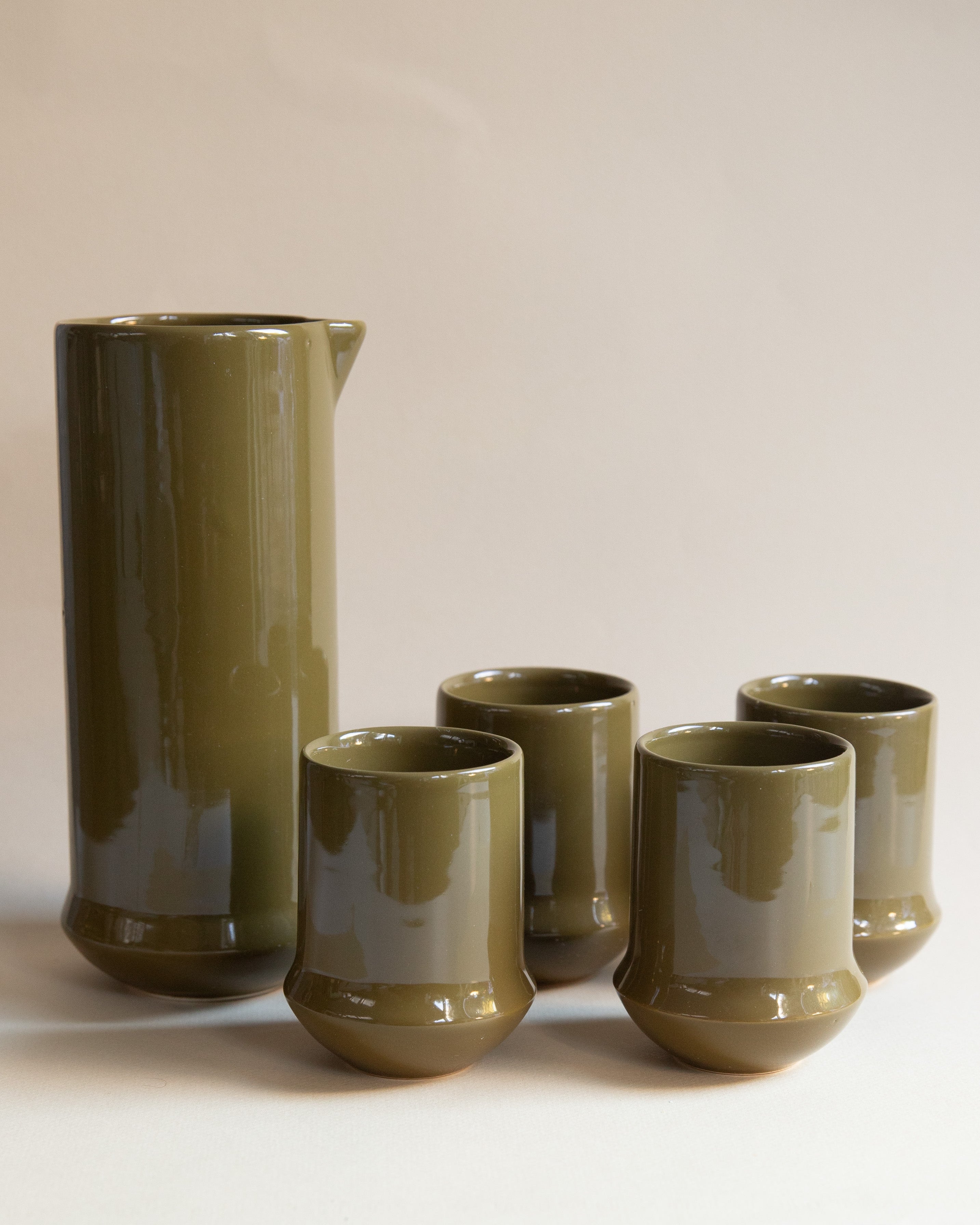 Set of olive green ceramic tumblers and a pitcher on a white background