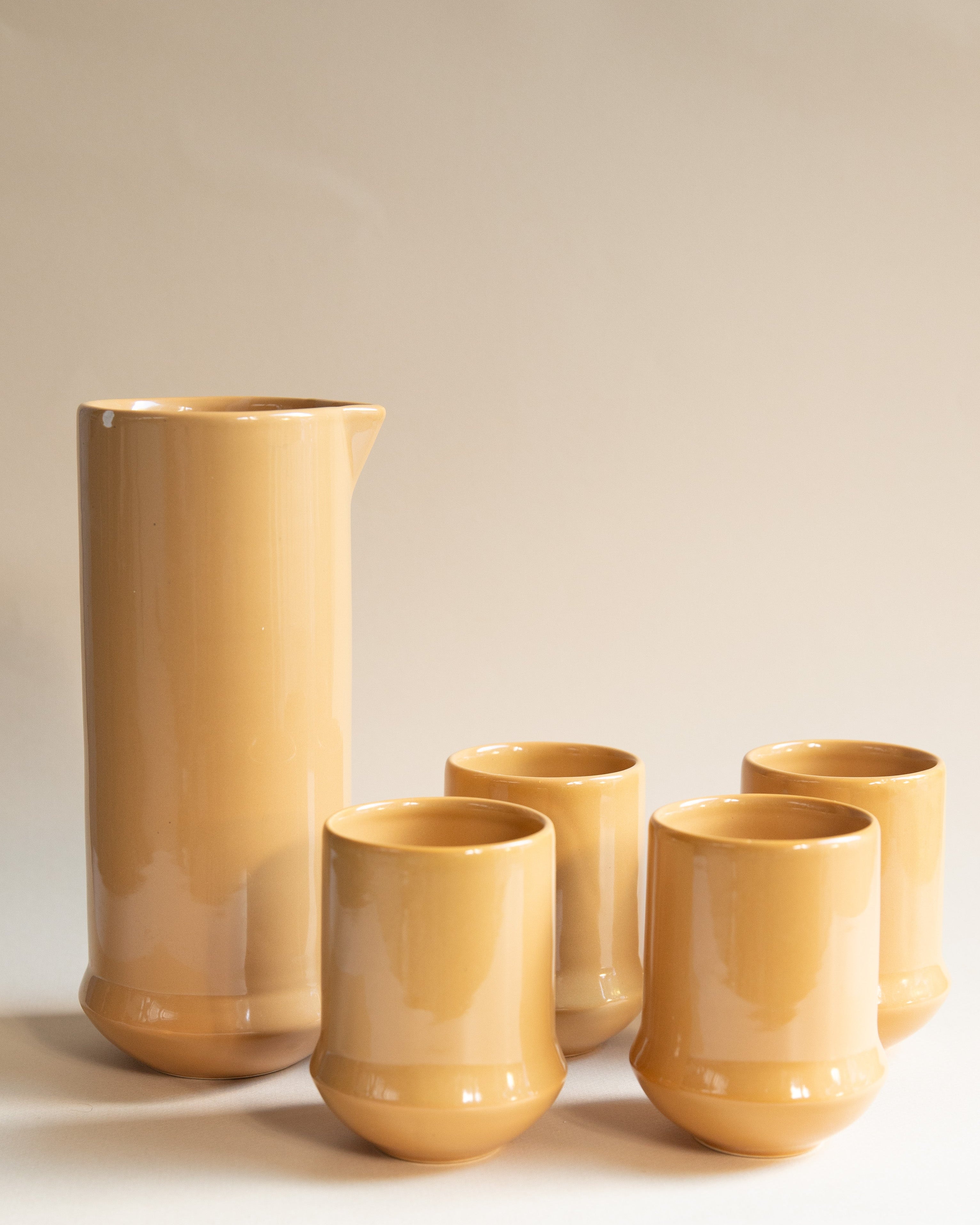 Set of yellow ceramic tumblers and a pitcher on a beige background