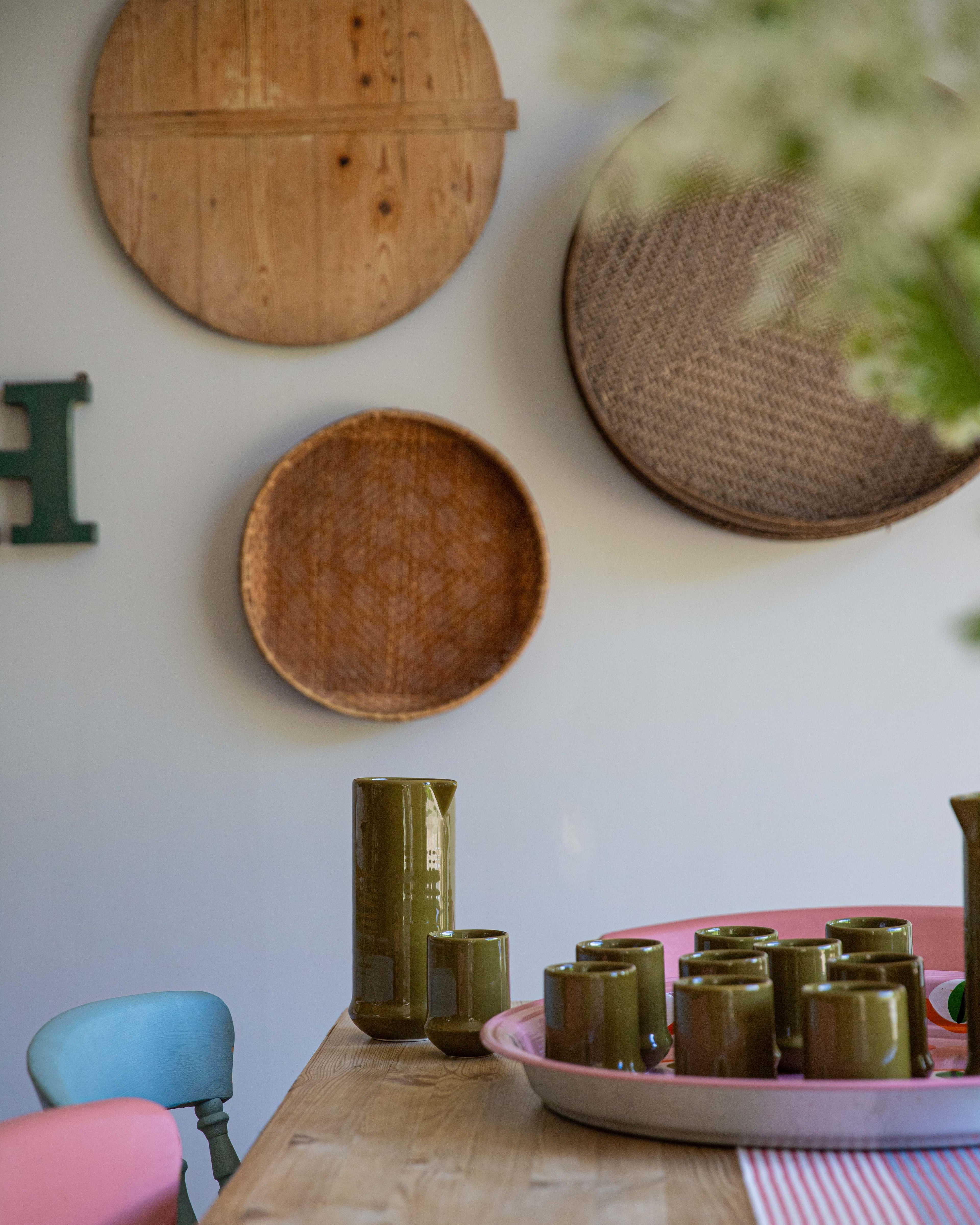 Decorative setting with wooden plates, green vases, and a pink chair on a table.